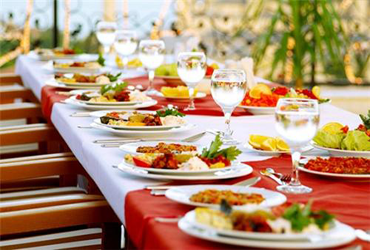 A beautiful table looks overflowing with dishes of delicious food and glasses of refreshing beverages