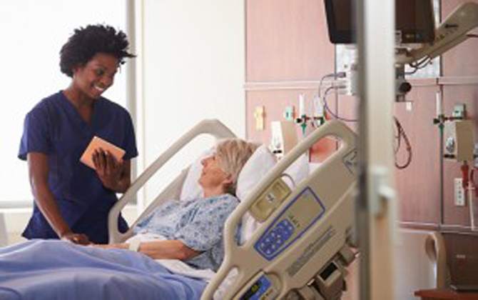 A nurse providing critical-care support talks attentively with a senior citizen in a hospital bed