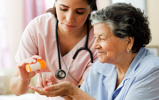 A healthcare professional giving home care to an elderly woman while holding a medicine glass