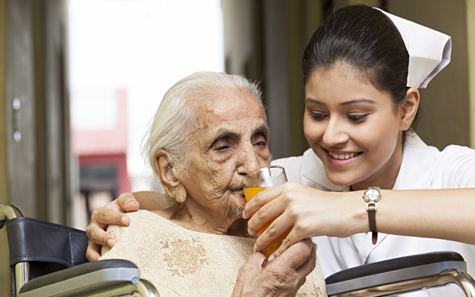 A care giver offers an older woman a drink of orange juice, improving wellness with care and love.