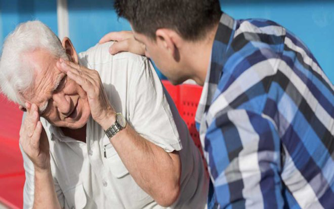 A man showing signs of distress by holding his head, while another man observes, in a context related to stroke care
