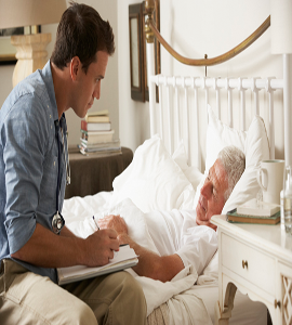 A man notes the condition of an old patient who has fallen ill and is laying on a bed.
