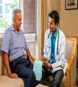 A home doctor discussing medical treatment with an elderly man with care while seated in a chair.