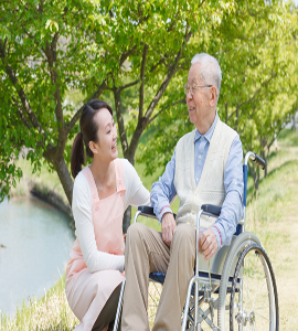 A personal home taker converses with an old woman who is sitting in a wheelchair with care and love.