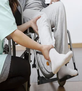 A nurse assisting a woman in a wheelchair, arranging her legs on the chair a nurse supports a woman