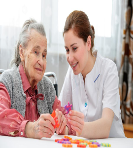 An elderly woman is receiving help from a nurse to solve a puzzle, showing kindness and patience