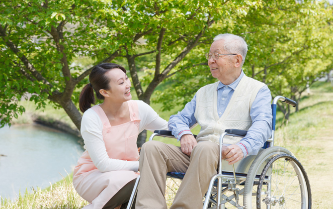 A woman kindly assists an elderly man in a wheelchair, providing physical disability home care services